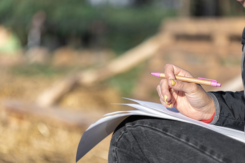 A woman's hand holds a pen and sheets of paper, copy space.