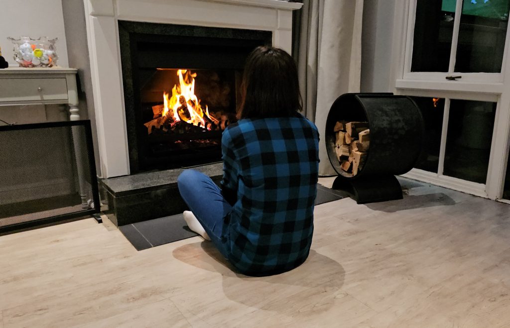 Lonely sad woman looking at the fire in the fireplace in the living room.